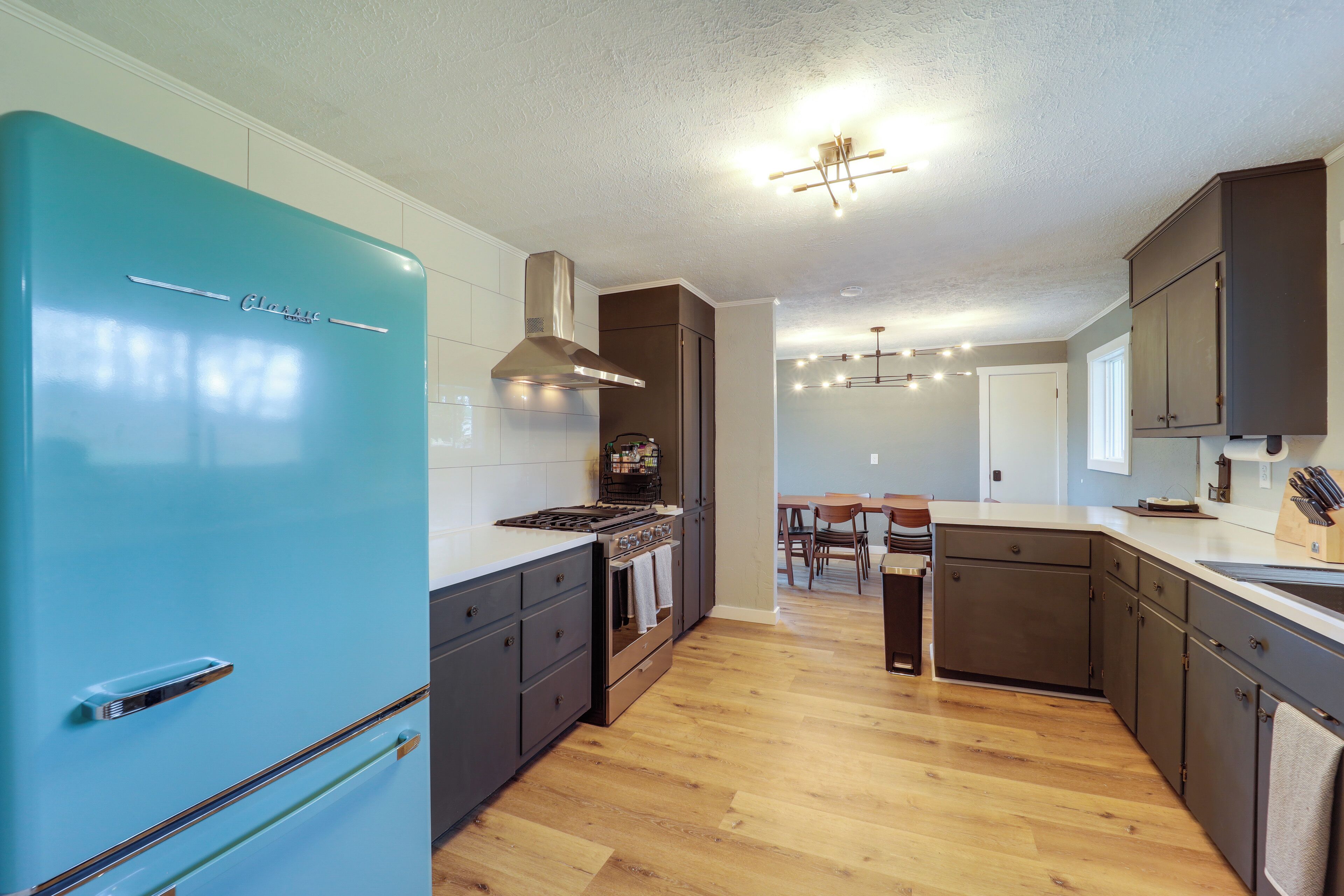 A modern kitchen with a teal refrigerator, dark cabinetry, and a wooden floor.