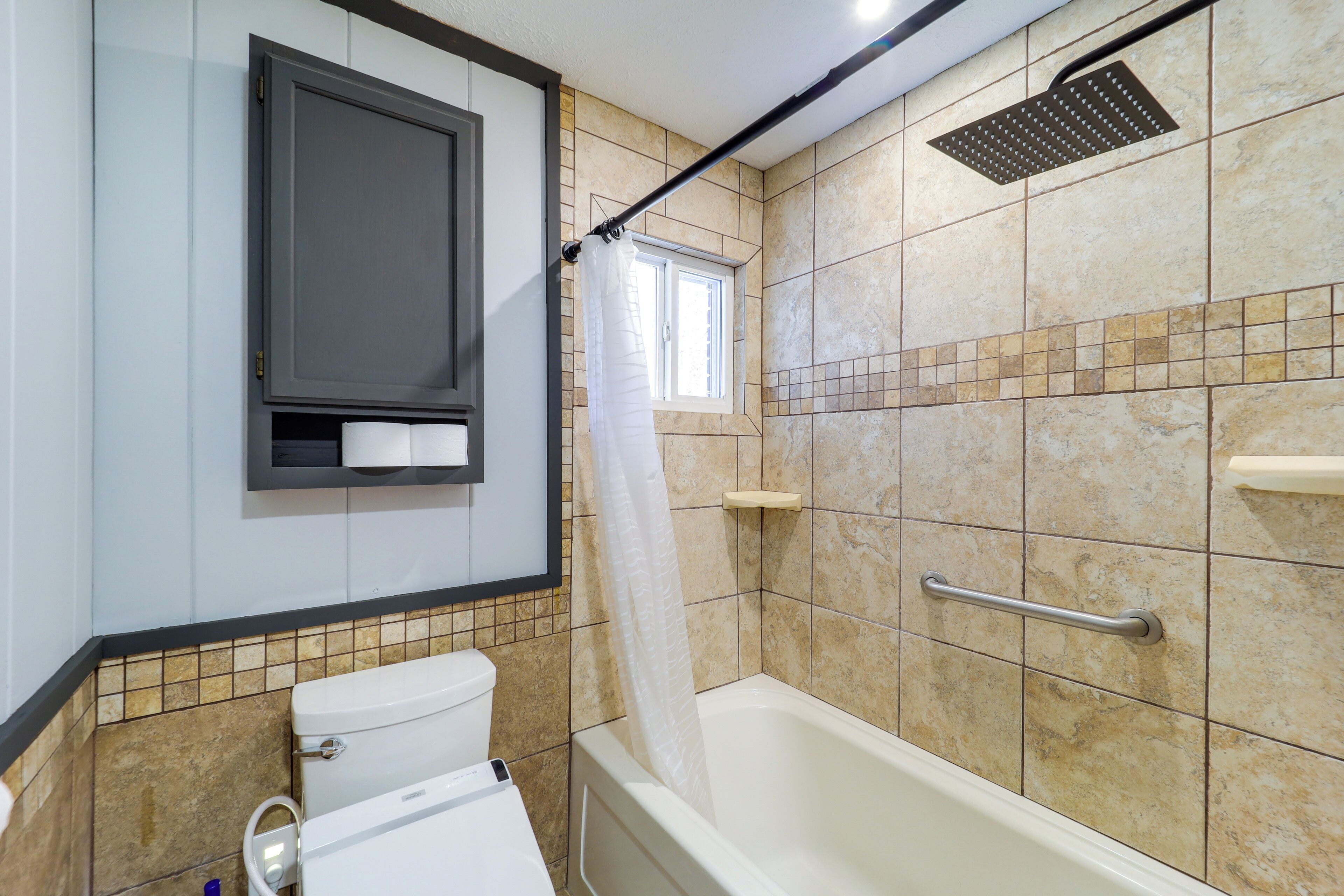 A bathroom with a toilet, bathtub, shower, and a window.