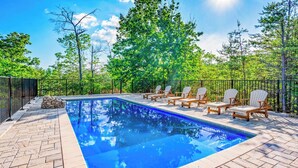 Ein Swimmingpool mit Liegestühlen und einem Steinhaufen, umgeben von einem Zaun und Bäumen.