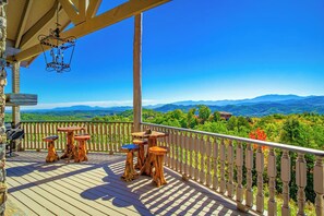 Une terrasse en bois avec des tables et des chaises, une rambarde et une vue sur les montagnes.