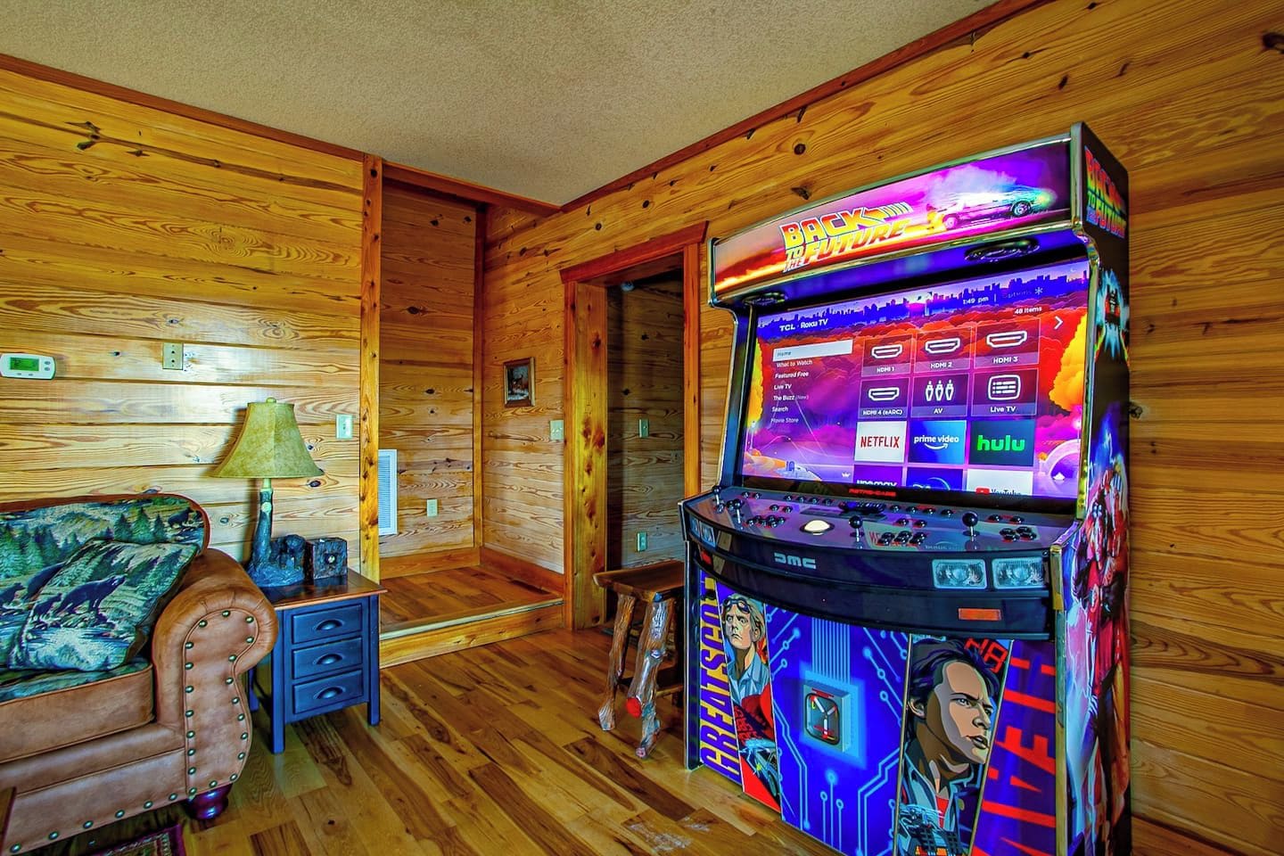 A room with wooden walls, a couch, a lamp, and a gaming console with a colorful display.