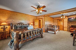 A log cabin interior with a rustic bed, a fireplace, and a ceiling fan.