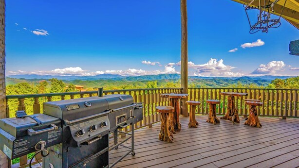 Eine Terrasse im Freien mit einem Grill und Holzsesseln, mit Blick auf eine gebirgige Landschaft.