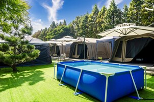 Un camping con varias tiendas de campaña y una piscina inflable azul.