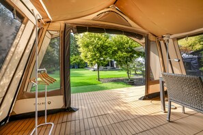 A tent with a view of a green lawn and trees.