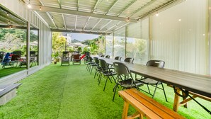 A covered outdoor area with a long table and chairs, artificial grass, and a view of the surrounding landscape. - L.M.S B&B GLAMPING (Gongguan)