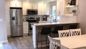 Una cocina moderna con electrodomésticos de acero inoxidable, una isla central con taburetes y un comedor con sillas blancas.