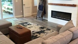 Una sala de estar moderna con un sofá seccional, una chimenea, un televisor montado en la pared y una escalera apoyada contra la pared.