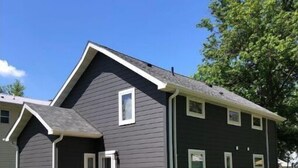 Una casa de dos pisos con fachada gris oscuro, un porche con barandillas de madera y un césped cuidado.