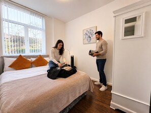 Un dormitorio con una cama, almohadas, una maleta y una persona empacando.