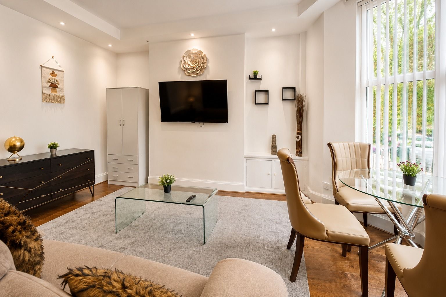 A modern living room with a flat-screen TV, a glass coffee table, a sofa, and a dining area with a glass table and chairs.