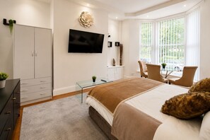 Ein modernes Schlafzimmer mit Bett, Fernseher, Schreibtisch und Stuhl.