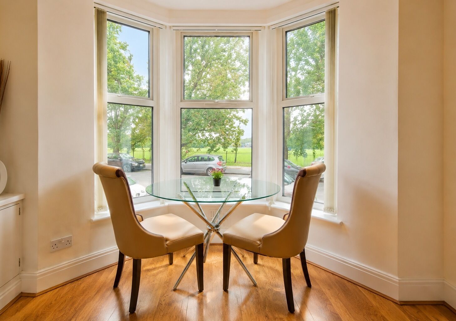 Habitación de esquina con una mesa de vidrio y dos sillas, ventanas amplias y vista a la calle.