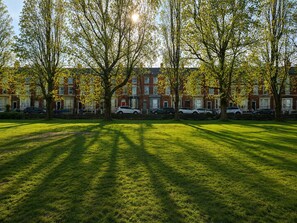 A grassy area with trees and parked cars in front of a row of red brick townhouses. - Botanic Gardens Oasis: Urban Convenience & Comfort (Liverpool)