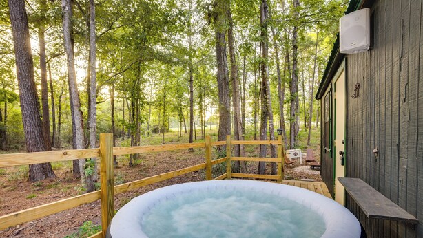 A hot tub in a wooded area with a wooden deck and a building in the background. - Cozy Onalaska Cabin ~ 2 Mi to Lake Livingston! (Onalaska)