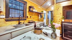 A compact kitchen with wooden walls, a sink, a stove, and a coffee maker. - Cozy Onalaska Cabin ~ 2 Mi to Lake Livingston! (Onalaska)