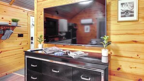 A wooden interior with a large flat-screen TV mounted on the wall, a black entertainment unit with magazines, and two small potted plants. - Cozy Onalaska Cabin ~ 2 Mi to Lake Livingston! (Onalaska)