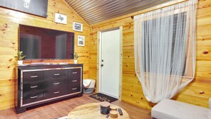 A wooden cabin interior with a large TV, a wooden cabinet, a round table with a plant, and a sofa. - Cozy Onalaska Cabin ~ 2 Mi to Lake Livingston! (Onalaska)