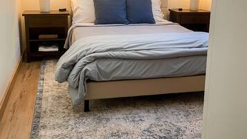 A neatly made bed with a headboard, two bedside tables with lamps, and a patterned rug on a wooden floor.