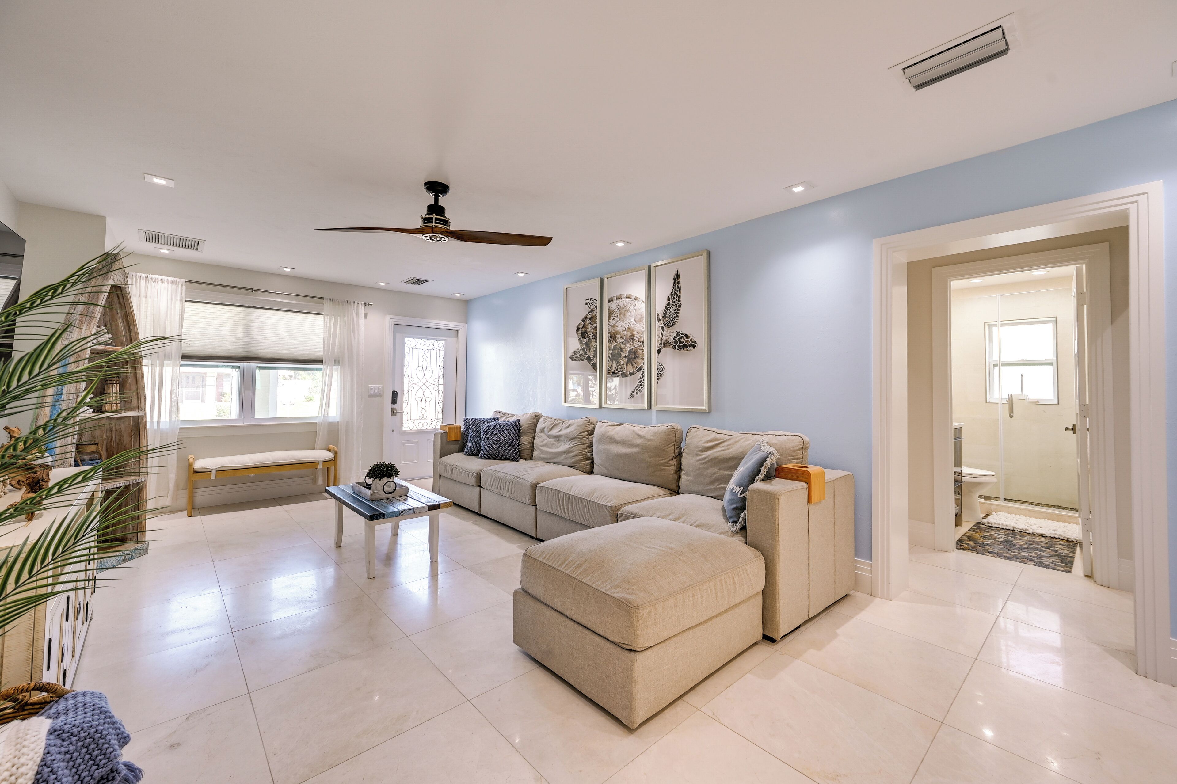 A spacious living room with a beige sectional sofa, a coffee table, and a ceiling fan.
