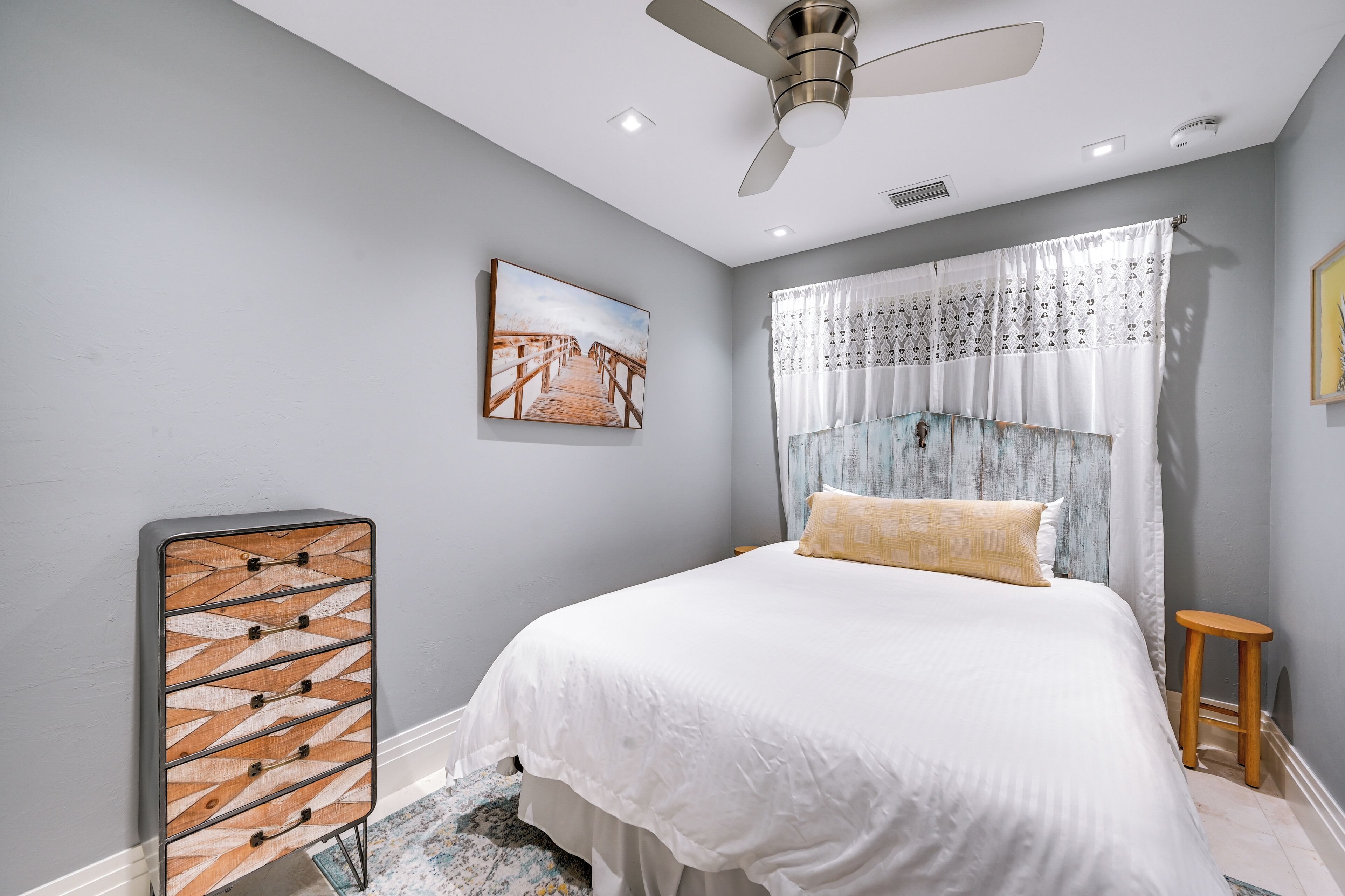 A bedroom with a bed, a ceiling fan, a picture on the wall, and a dresser.