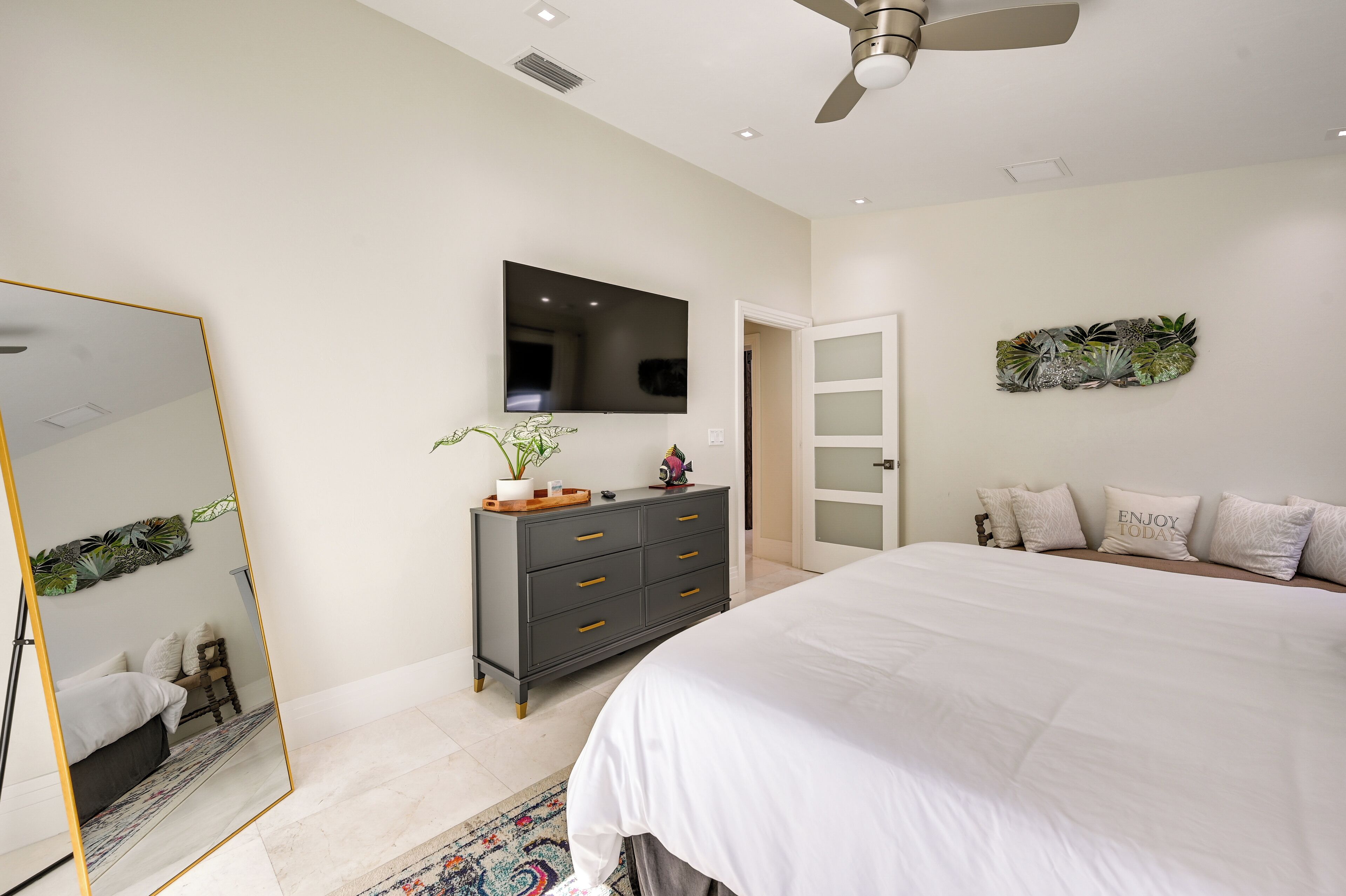 A modern bedroom with a large bed, a dresser, a flat-screen TV, and a ceiling fan.