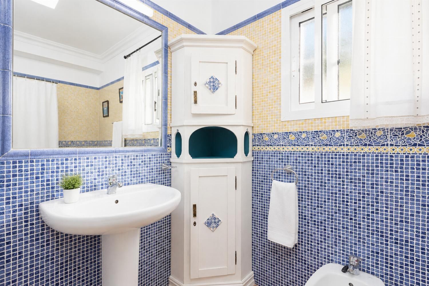 A bathroom with a white sink, a mirror, a cabinet with a decorative tile, and a towel rack.