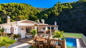 Une villa dotée d’un patio, de mobilier d’extérieur, d’une piscine et offrant une vue sur une colline boisée.