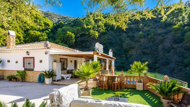Une villa dotée d’un patio, d’un espace salon extérieur et offrant une vue sur une colline boisée.