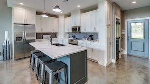 Una cocina moderna con armarios blancos, un refrigerador de acero inoxidable, un microondas y una isla grande con taburetes de bar.