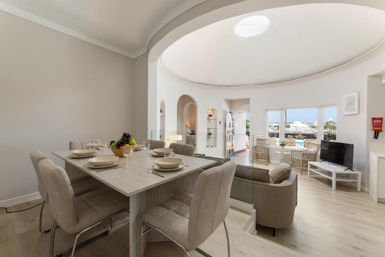 A modern dining area with a table set for four, a television, and a view of the outdoors.