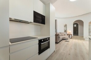 Cozinha moderna com eletrodomésticos embutidos, área de refeições com sofá e corredor que leva a uma porta.