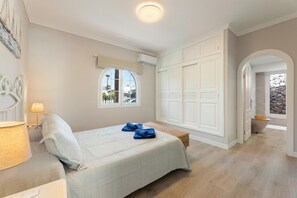 A bedroom with a bed, a bedside lamp, a window, a wardrobe, and a bathroom visible through an archway. - Villa Alisa - Three Bedroom Villa, Sleeps 6 (Tías)