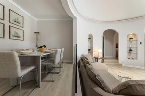 Uma sala de jantar moderna com uma mesa comprida, cadeiras e um sofá. Há quadros nas paredes e um abajur sobre a mesa.