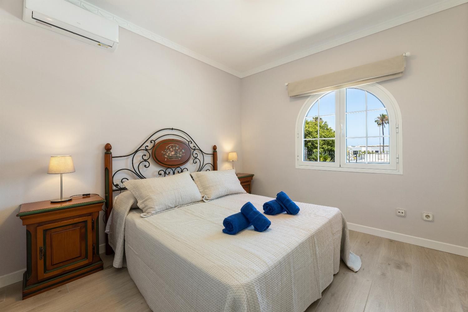 Un dormitorio con una cama, dos mesitas de noche, una ventana y un equipo de aire acondicionado.