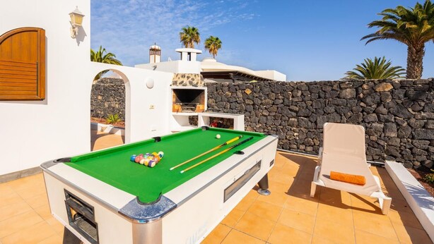 A pool table with balls, a lounge chair, and a stone wall.