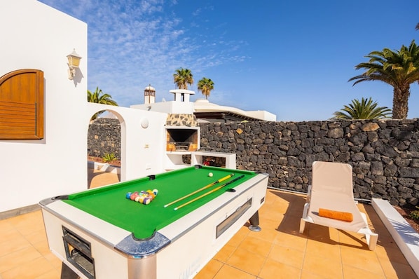 A pool table with balls, a lounge chair, and a stone wall.