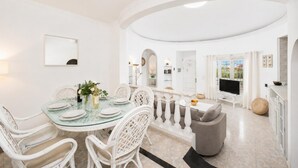 Un espace repas avec une table en verre, des chaises blanches et une vue sur l’extérieur.