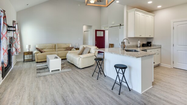 A spacious living area with a sofa, a small coffee table, and a kitchen with a countertop and stools. - Cape Charles Home: 4 Mi to Kiptopeke State Park! (Cape Charles)
