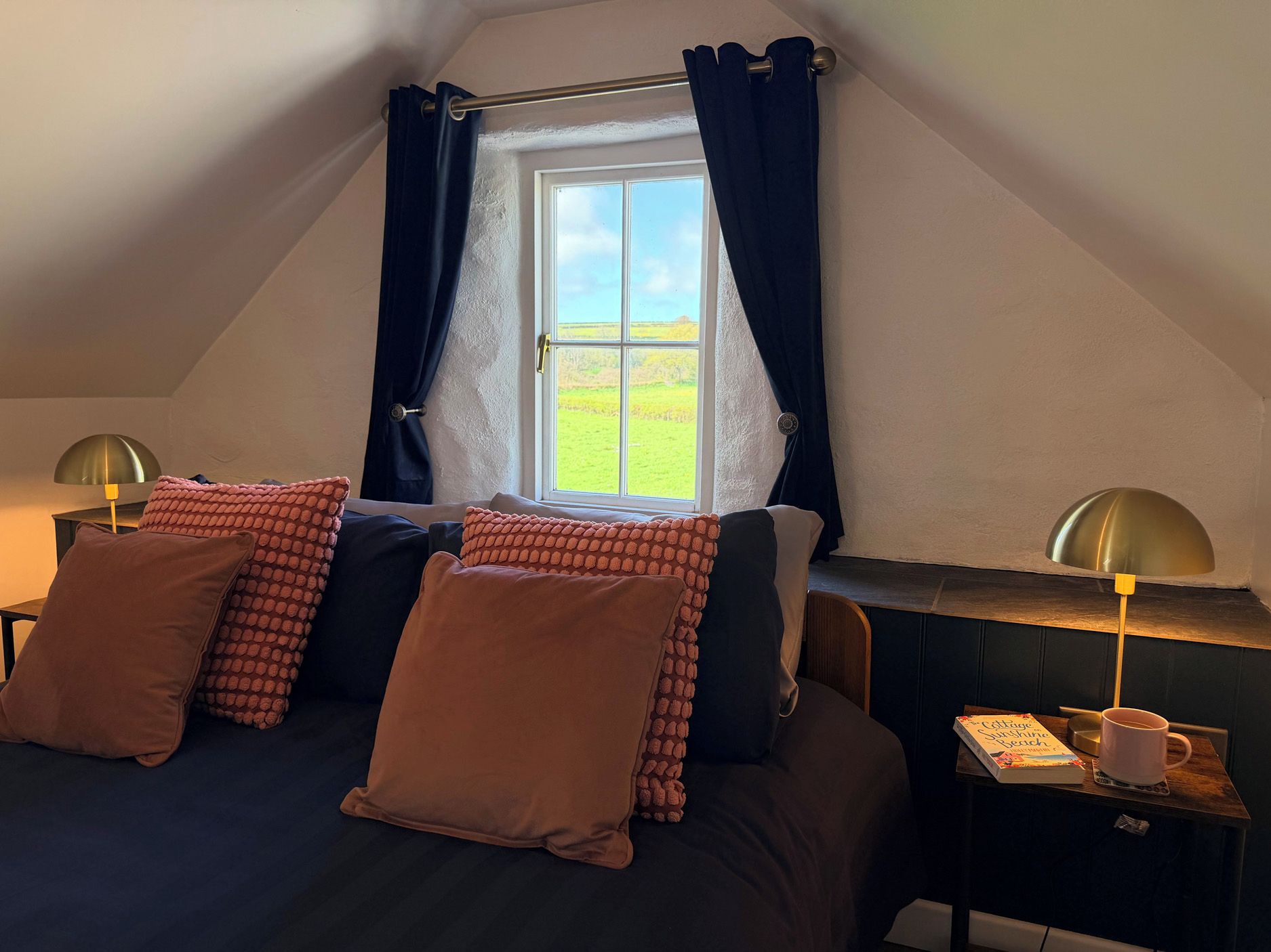 Un dormitorio acogedor con cama, dos mesitas de noche, ventana con cortinas y vista a un campo verde.