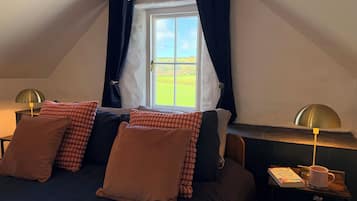 Ein gemütliches Schlafzimmer mit einem Bett, zwei Nachttischen, einem Fenster mit Vorhängen und Blick auf ein grünes Feld.