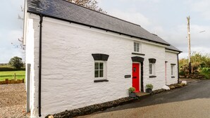 A white building with a red door, a black roof, and a gravel driveway. - Pensarngerrig (Llandysul)