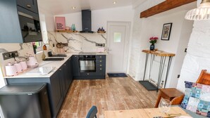 A modern kitchen with dark cabinets, a built-in oven, and a marble backsplash. - Pensarngerrig (Llandysul)