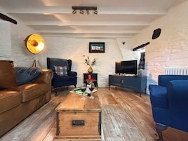A living room with a brown leather sofa, a blue armchair, a wooden coffee table with a board game, a TV on a stand, and a painting on the wall.