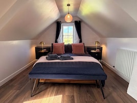 A bedroom with a large bed, two bedside tables with lamps, a window with curtains, and a radiator.