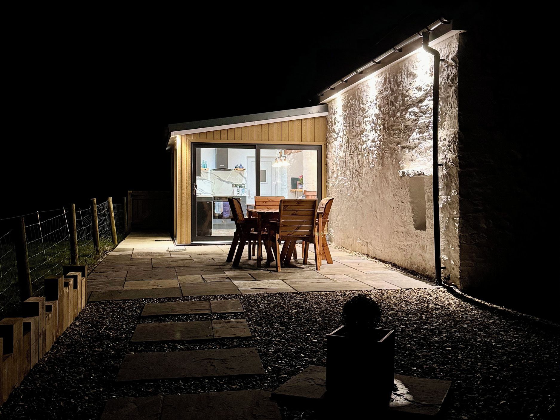 Un espace extérieur aménagé avec une table et des chaises, un chemin en pierre et un bâtiment doté d’une porte en verre.