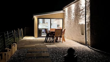 Un espace extérieur aménagé avec une table et des chaises, un chemin en pierre et un bâtiment doté d’une porte en verre.