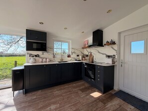 A modern kitchen with dark cabinetry, a marble backsplash, and a large window. - Pensarngerrig (Llandysul)