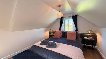 Une chambre à coucher avec un grand lit, deux tables de chevet, une fenêtre avec des rideaux et un luminaire suspendu.