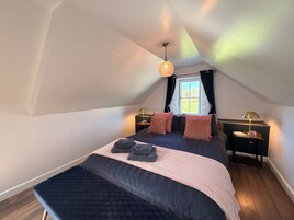 A bedroom with a large bed, two bedside tables, a window with curtains, and a hanging light fixture.
